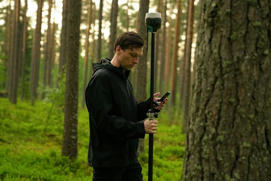 Mann in der Natur scannt mit einem Gerät neben einem Baum.