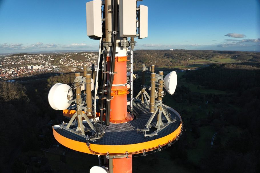 Antennenmast mit mehreren Sendeeinheiten auf einer Plattform, Aussicht auf eine ländliche Umgebung.